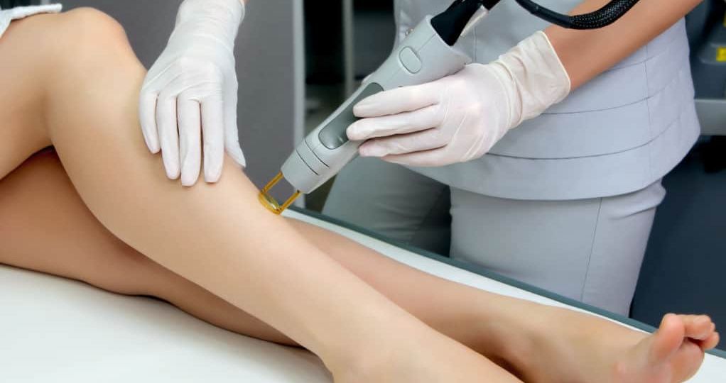 Professional performing laser hair removal on a client's leg